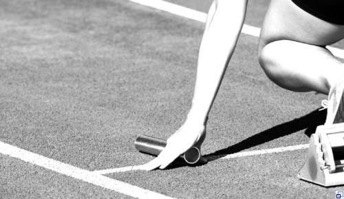 Leichtathlet Sportler im Stadion, mit einem Fuß im Startblock und Staffel in der Hand