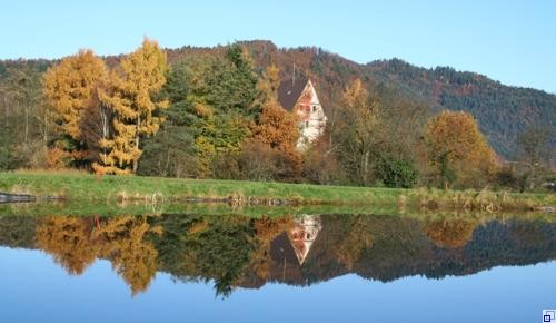 Turmspitze des Gröbernturm spiegelt sich im Wasser davor, hintendran Wald und Berge